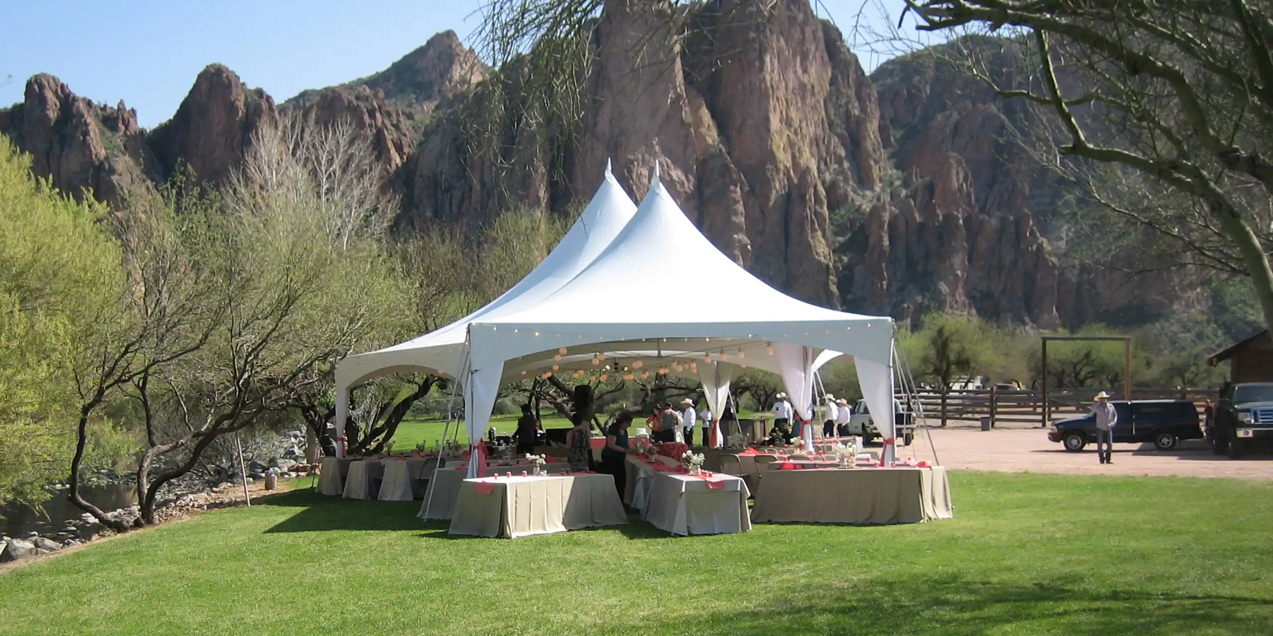 White outdoor event tent set on a green lawn with banquet tables, with rugged desert mountains in the background.