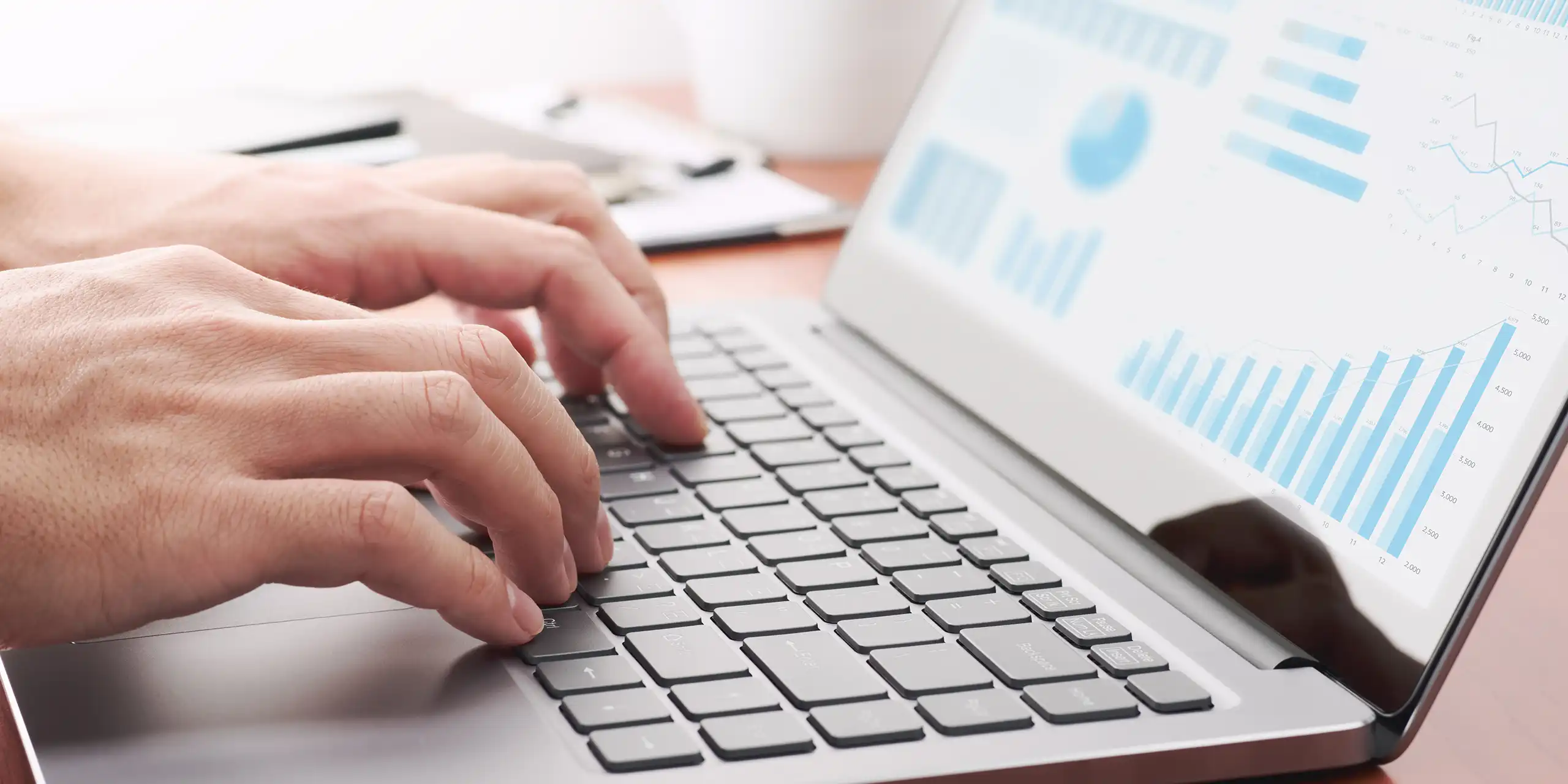 Hands typing on a laptop with analytics charts—ecommerce performance tracking and optimization.